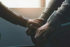 Close-up of someone's reaching out to put their hand on someone else's hands in a comforting way. Near window with low light environment.