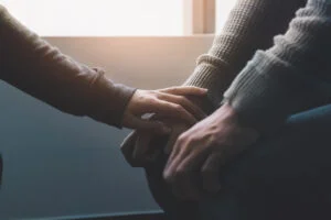 Close-up of someone's arm reaching out to hold another person's hands in a comforting way. Near window with low light environment.